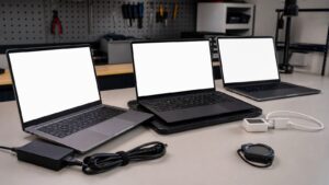 Three unbranded laptops with blank screens on a clean testing bench with chargers and measurement tools without readable markings.