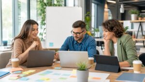 Business team collaborating around blank laptops, blank tablet, blank whiteboard, and unreadable sticky notes in a bright office.